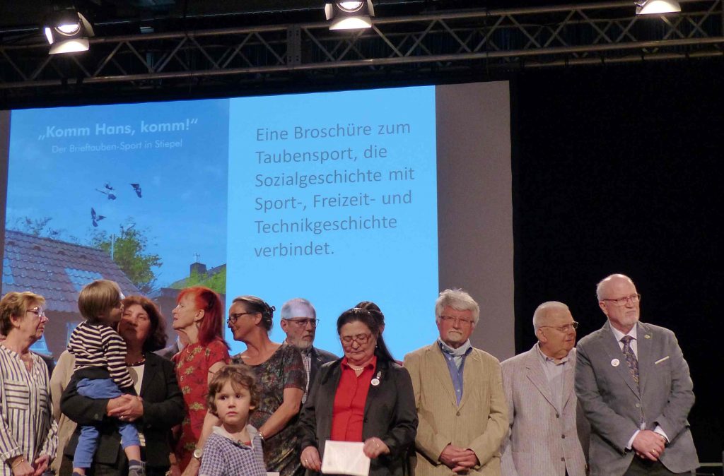 Vereinsmitglied Gerhard Hagenkötter (ganz rechts), im Hintergrund die Broschüre